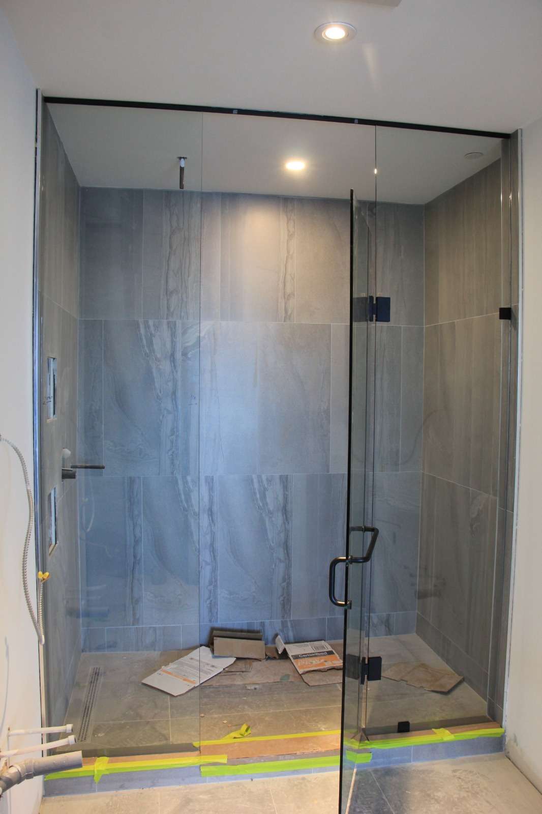 Frameless clear-glass shower enclosure with a black handle in a marble-tiled bathroom, during installation