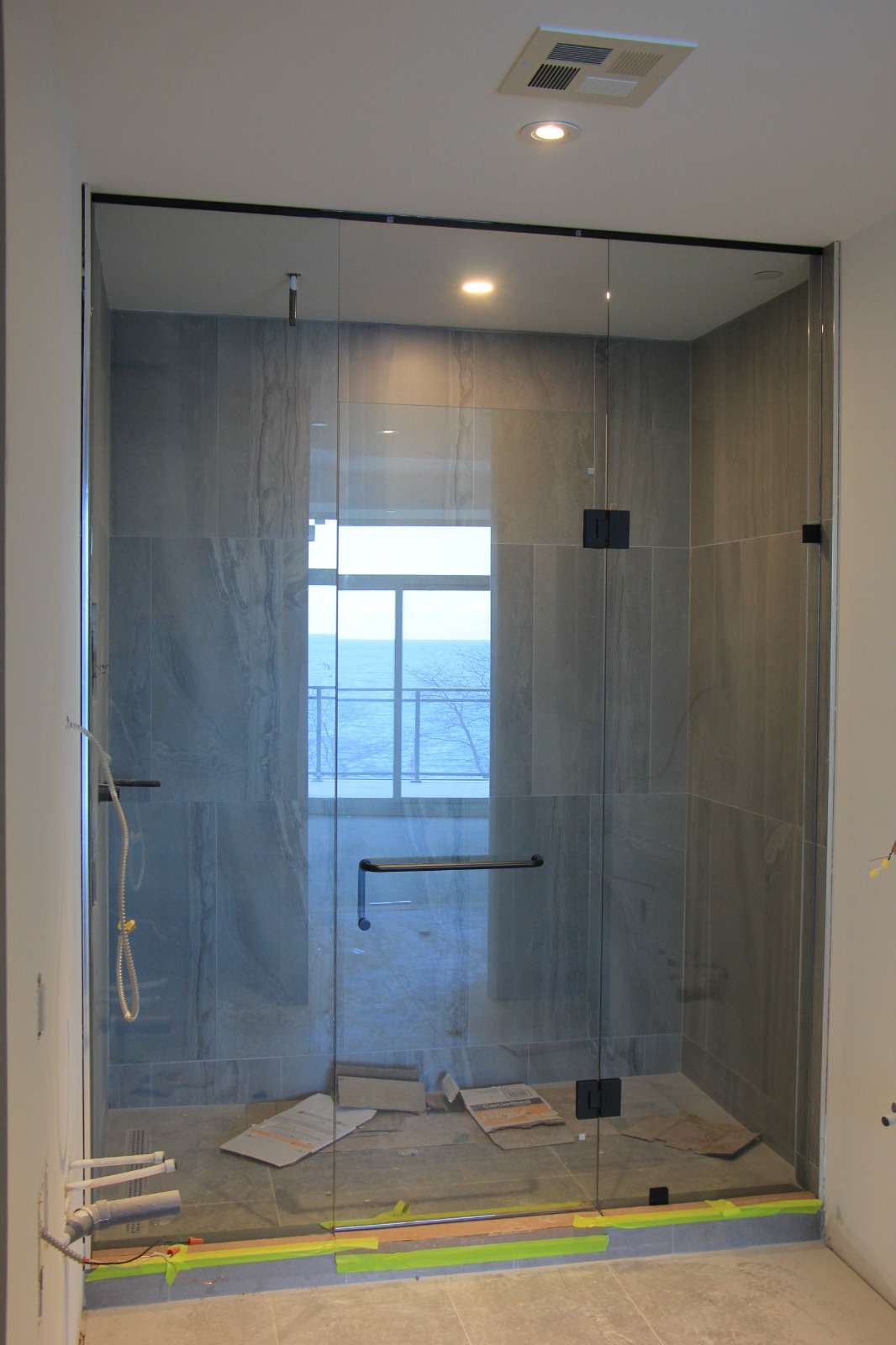 Frameless clear-glass shower enclosure facing a window, marble surround, before the final clean