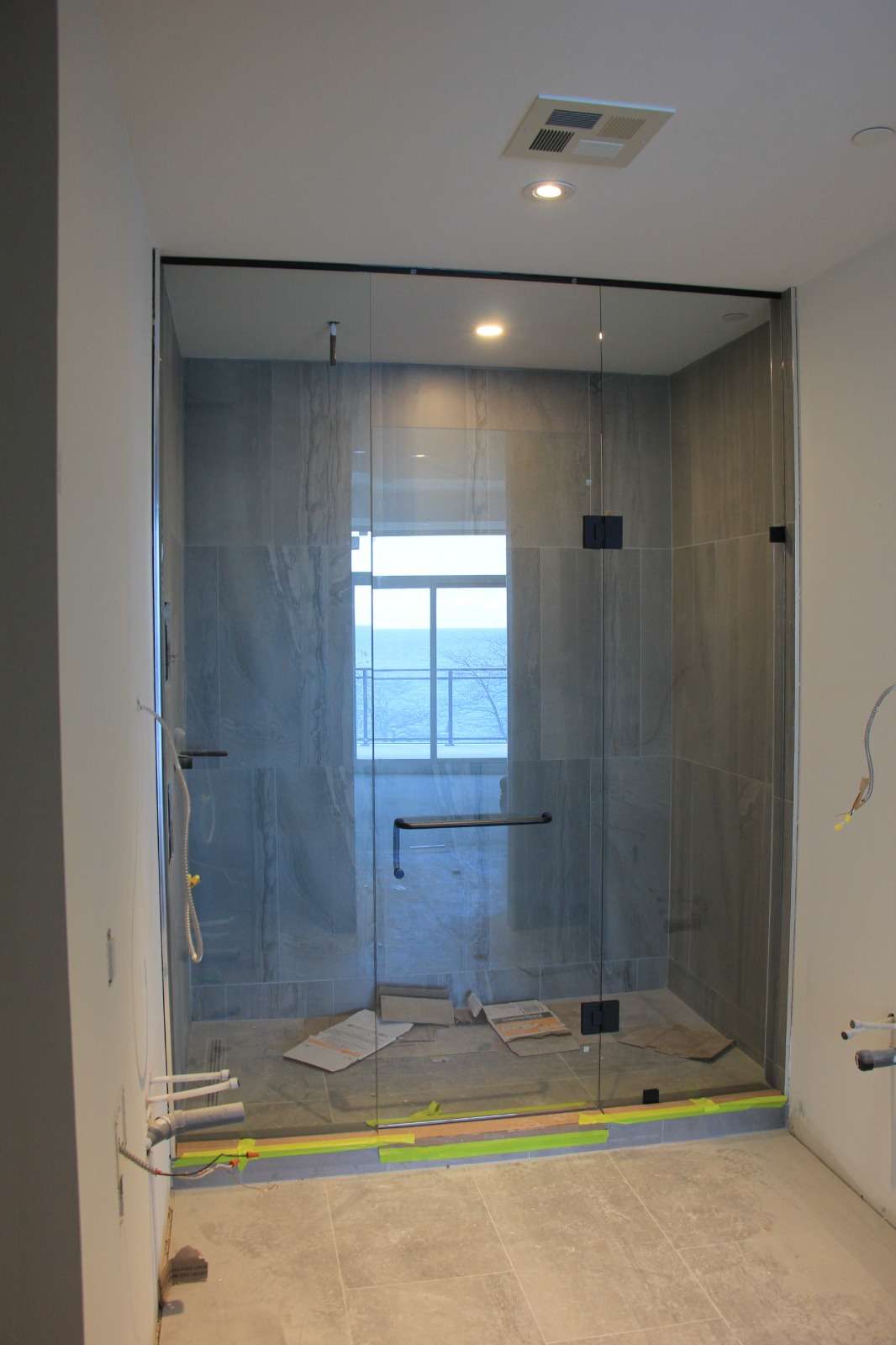 Clear frameless shower enclosure with a hinged door beside a window in a marble bathroom