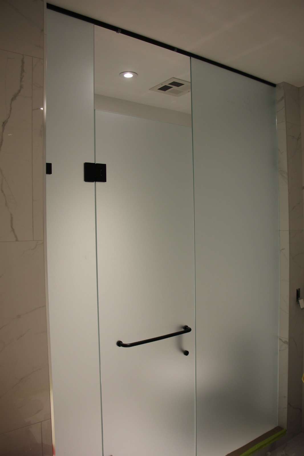 Close view of a frosted-glass shower door with a black bar handle