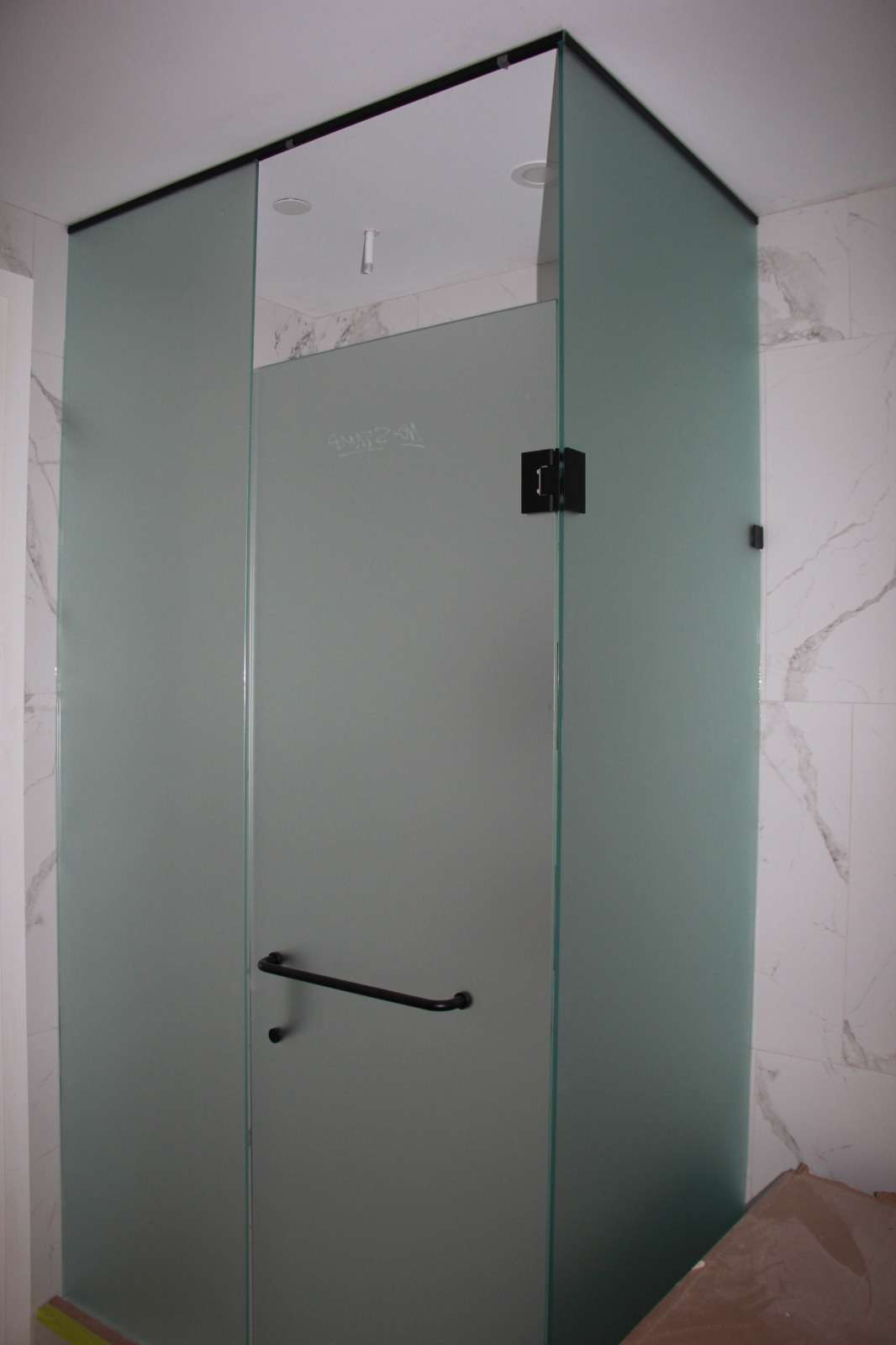 Frosted-glass shower enclosure with a bar handle, marble tile floor